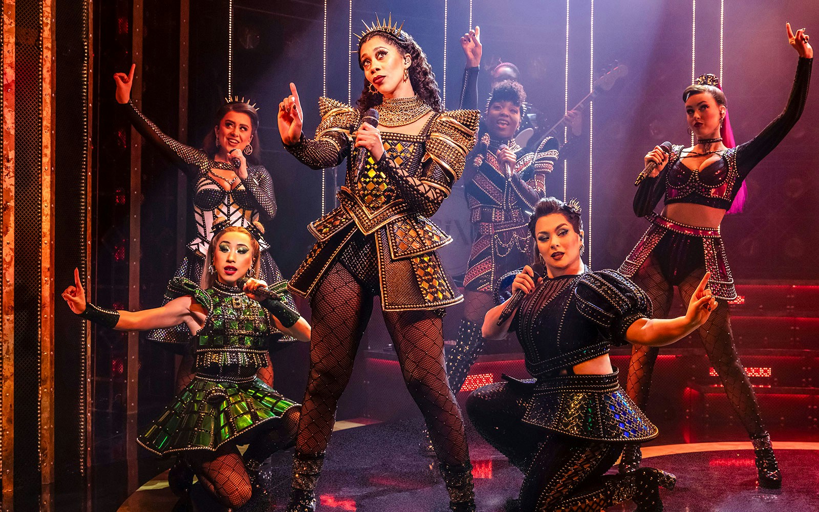 Performers in vibrant costumes on stage during the musical "Six.