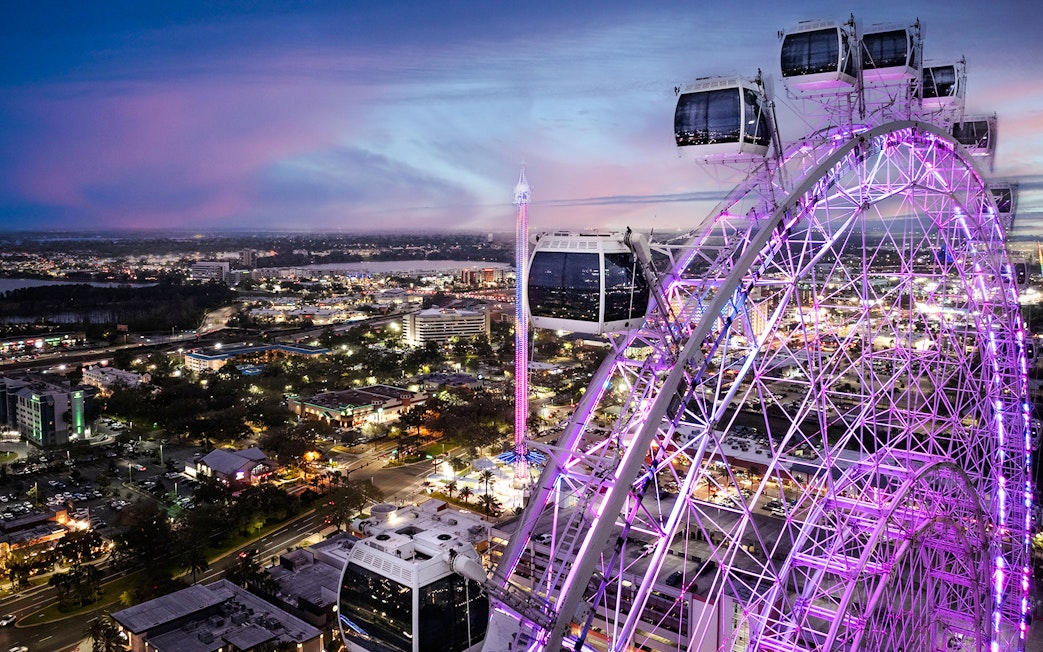 Ferris wheel at ICON Park, Orlando, illuminated at dusk with cityscape in the background.