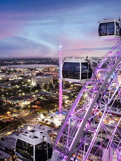 Ferris wheel at ICON Park, Orlando, illuminated at dusk with cityscape in the background.