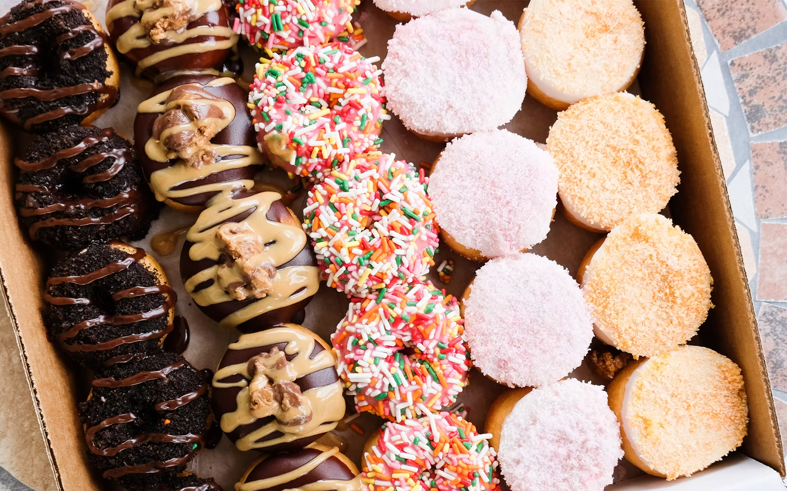 Assorted donuts with sprinkles, chocolate, and icing in a box.