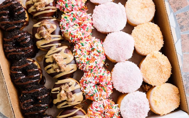 Assorted donuts with sprinkles, chocolate, and icing in a box.