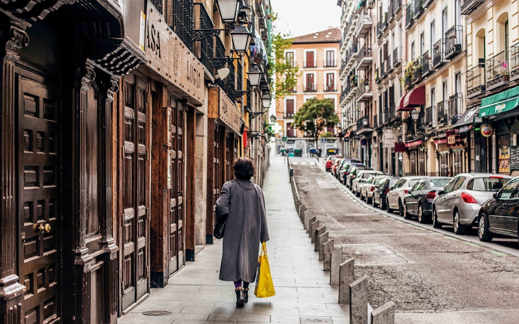 Street view in Barrio de La Latina, Madrid, with a person walking past traditional buildings.