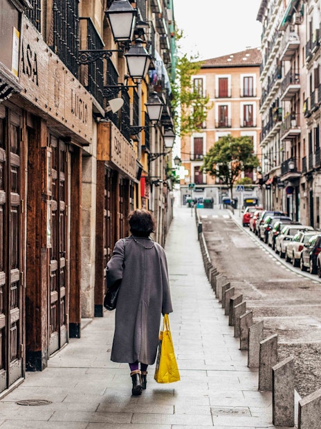 Street view in Barrio de La Latina, Madrid, with a person walking past traditional buildings.