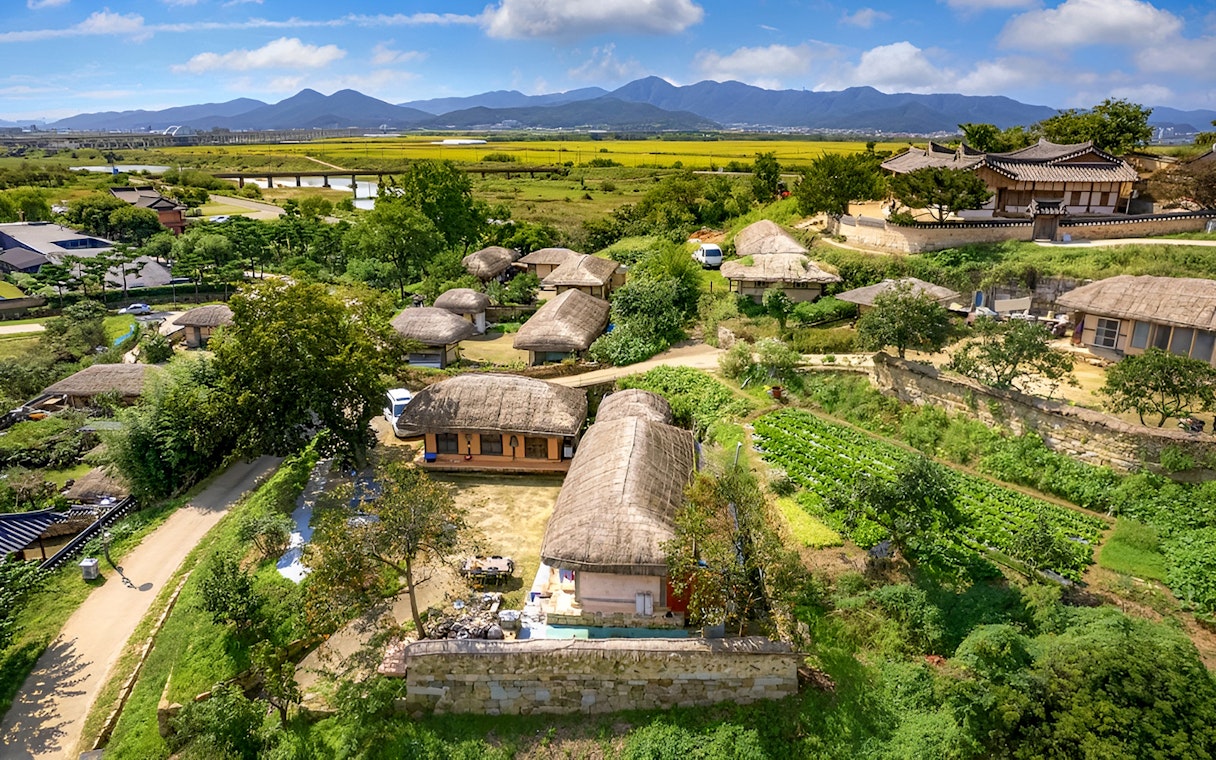 Traditional Korean village with thatched-roof houses in Gyeongju, surrounded by fields and mountains.