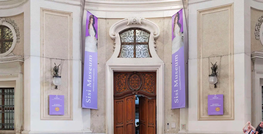 Entrance to the Sisi Museum with ornate wooden doors and purple banners.