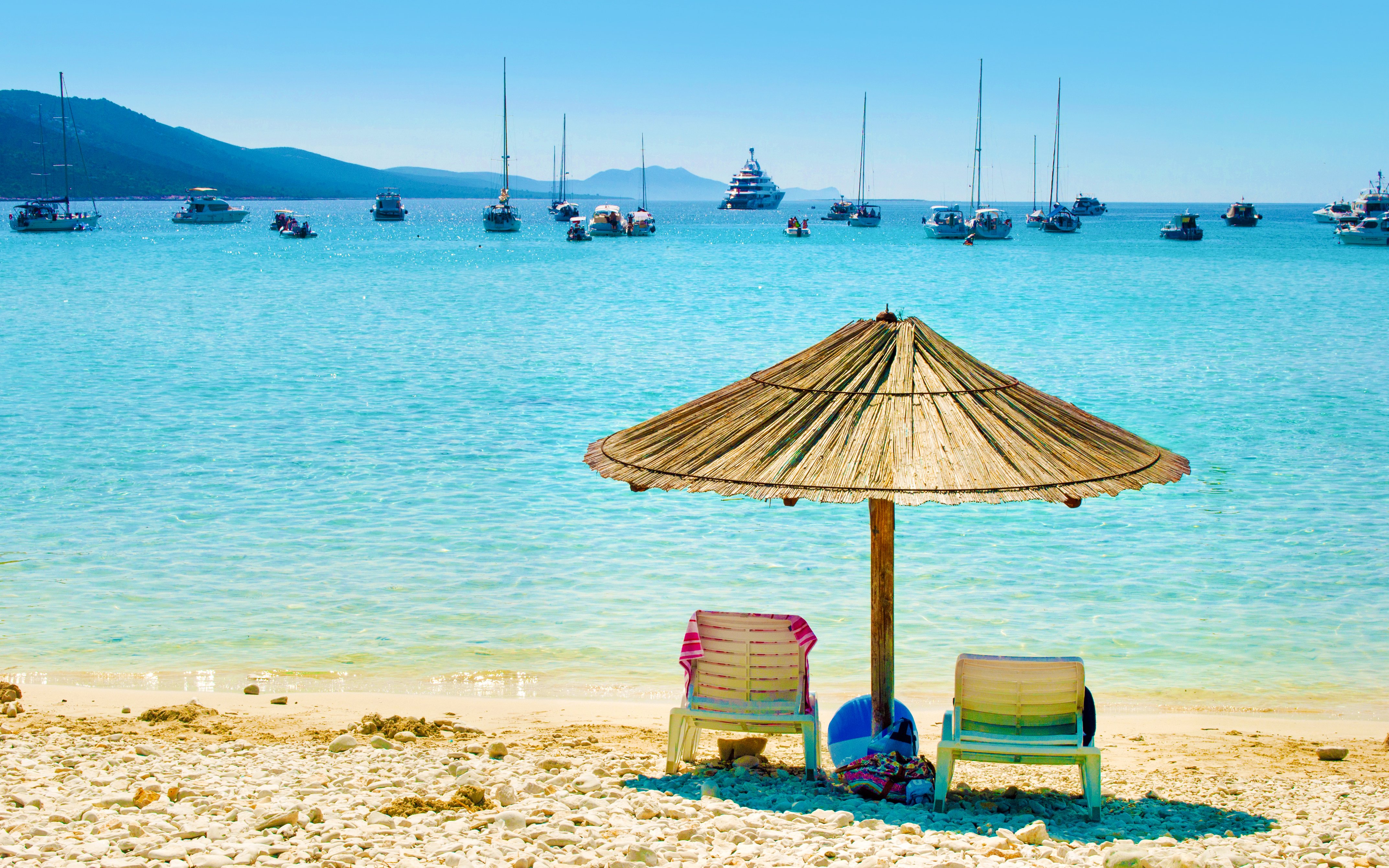 Sun loungers under a straw umbrella on Sakarun Beach, Croatia, with boats in the distance.