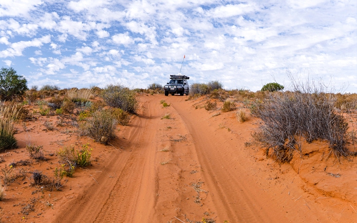4WD vehicle driving on sandy trail with shrubs on Moreton Island.