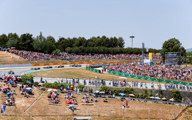 Formula 1 cars racing on Barcelona track with spectators in general admission area.