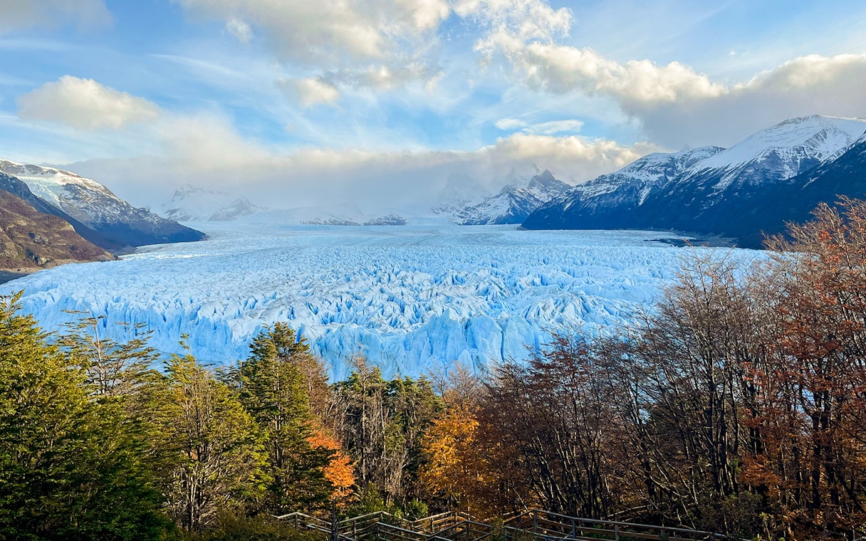 Perito Moreno Glacier in Argentina with surrounding mountains and autumn trees.