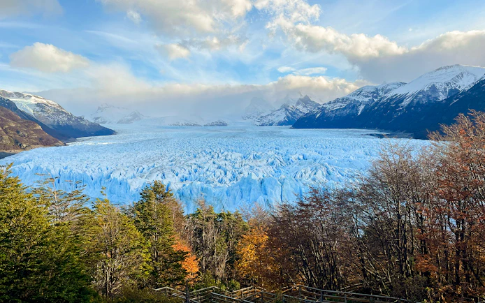 Perito Moreno Glacier in Argentina with surrounding mountains and autumn trees.