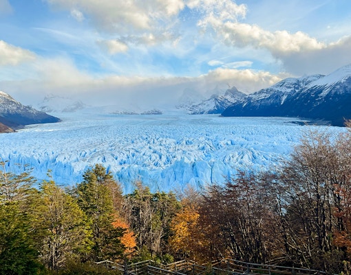 Perito Moreno Glacier in Argentina with surrounding mountains and autumn trees.