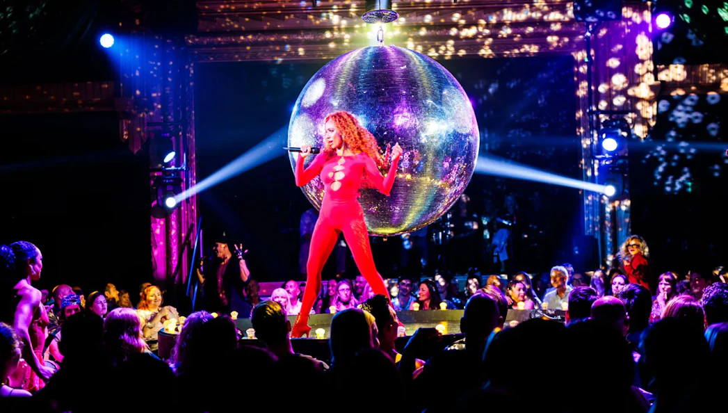 Performer in red outfit singing at La Ronde show, Sydney, with disco ball and audience.