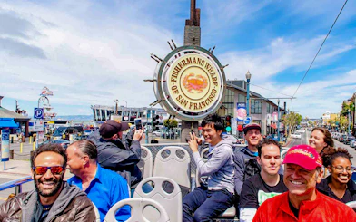 Open-top bus tour at Fisherman's Wharf, San Francisco, with tourists enjoying the view.