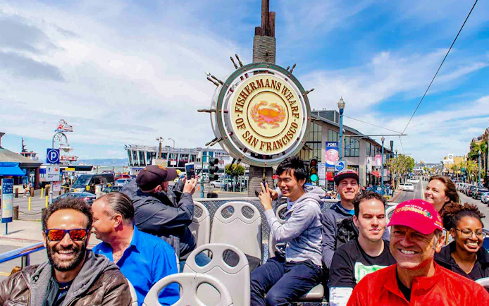 Open-top bus tour at Fisherman's Wharf, San Francisco, with tourists enjoying the view.