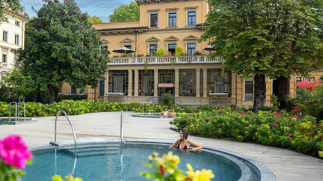 Outdoor spa pool at QC Terme Torino with historic building and lush gardens.