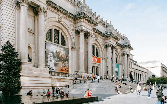 Exterior of The Metropolitan Museum of Art, New York City, with visitors on steps.