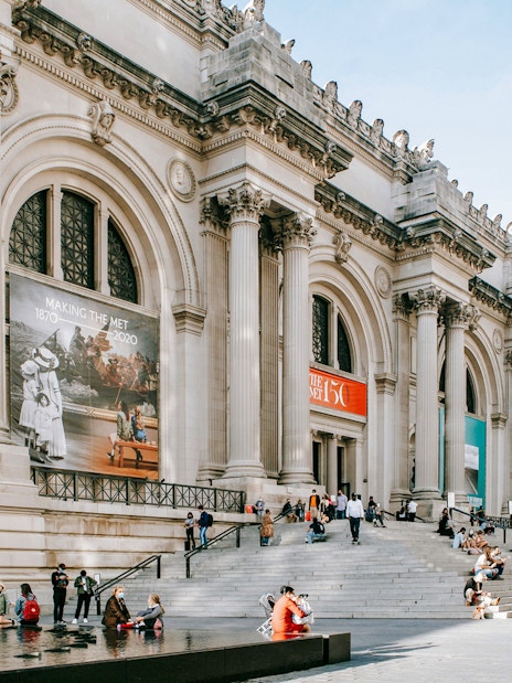 Exterior of The Metropolitan Museum of Art, New York City, with visitors on steps.