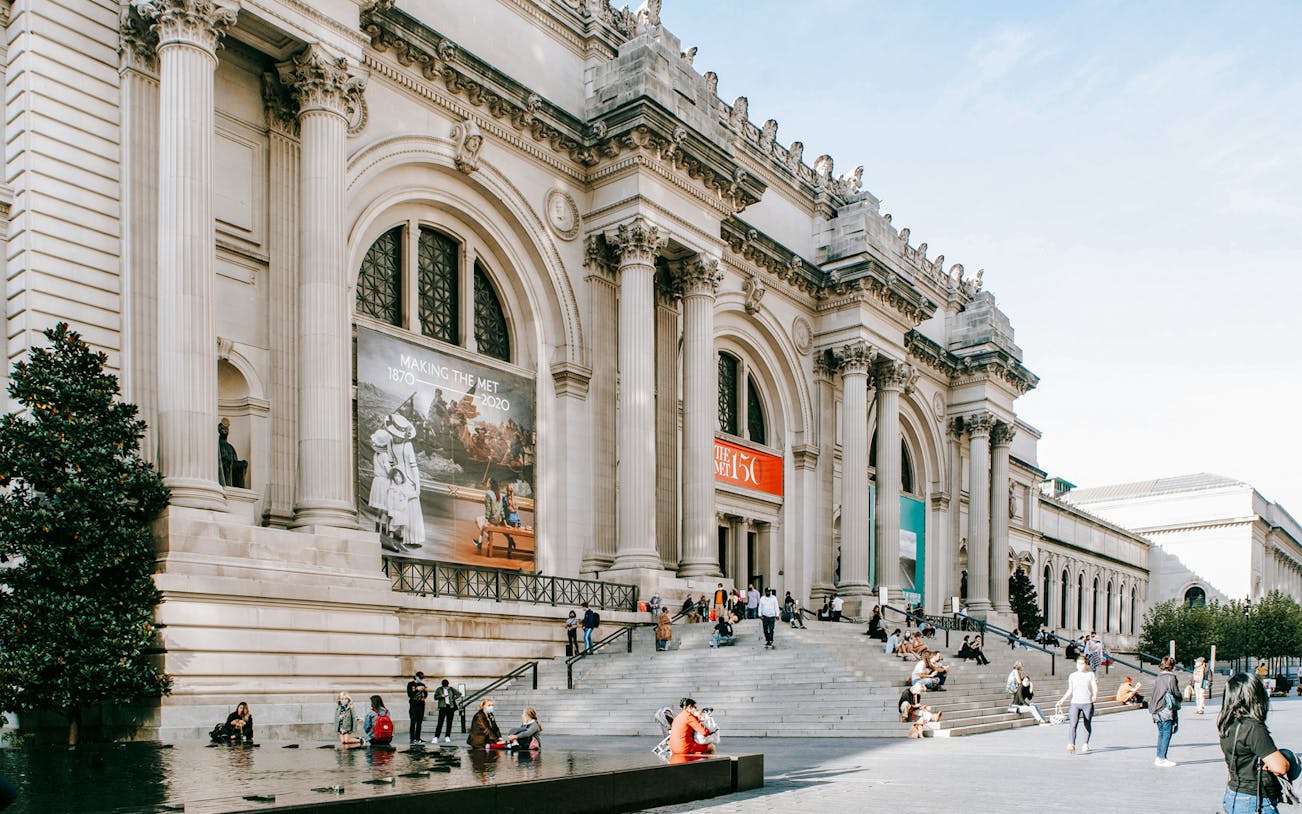 Exterior of The Metropolitan Museum of Art, New York City, with visitors on steps.