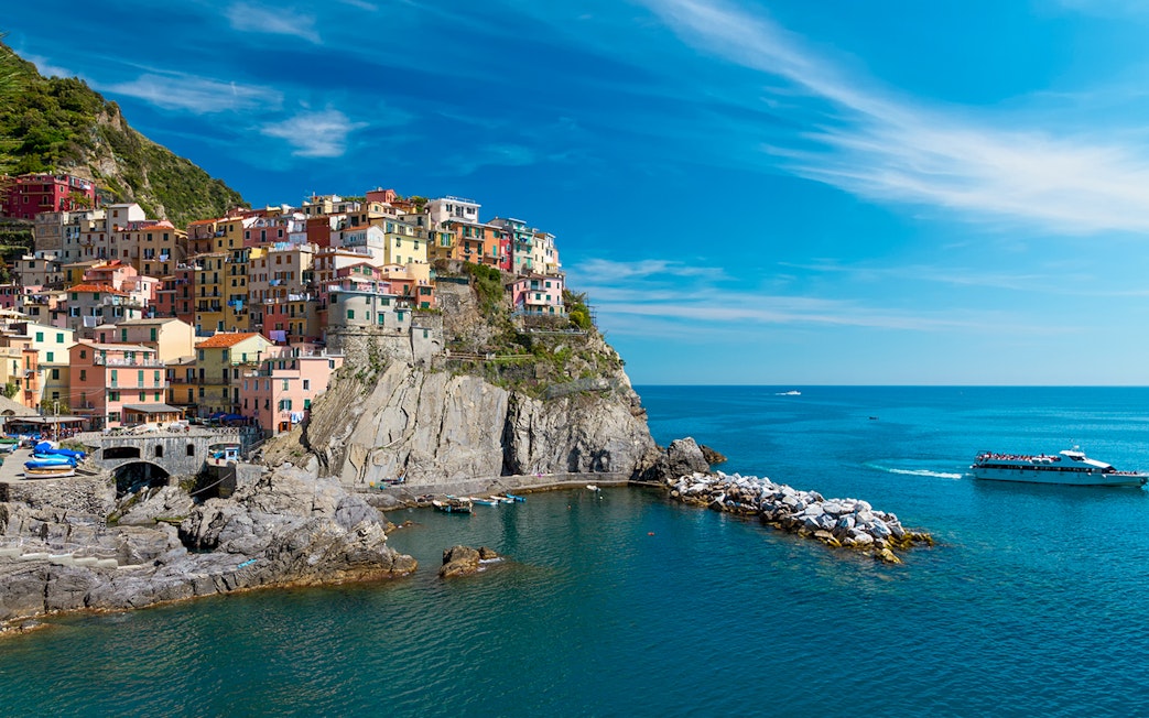 Colorful houses on a cliff in Cinque Terre with a boat in the sea, part of Florence to Cinque Terre tour.