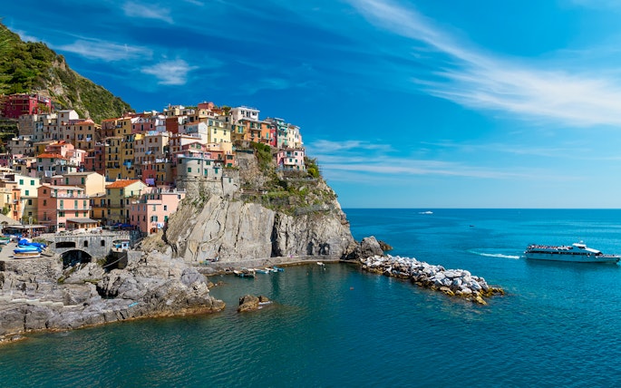 Colorful houses on a cliff in Cinque Terre with a boat in the sea, part of Florence to Cinque Terre tour.