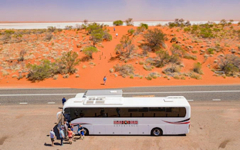 Tour bus with travelers in red desert landscape near Alice Springs, Australia.