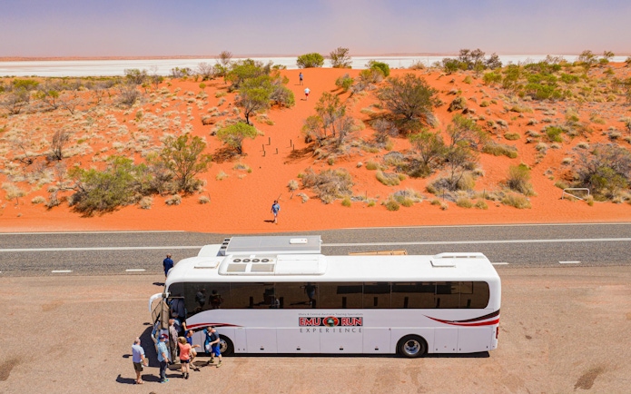 Tour bus with travelers in red desert landscape near Alice Springs, Australia.