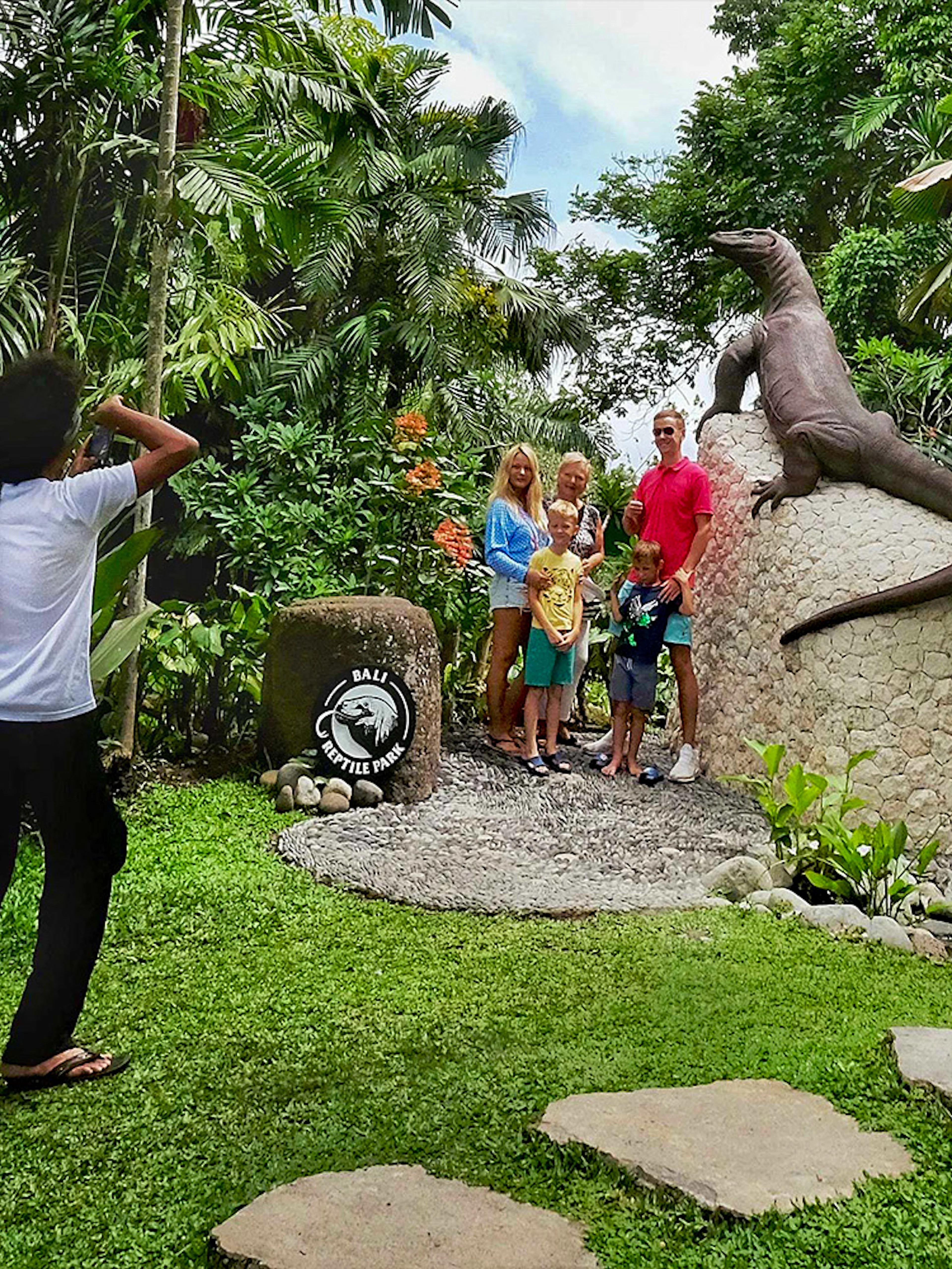 Family posing by Komodo dragon statue at Bali Reptile Park.