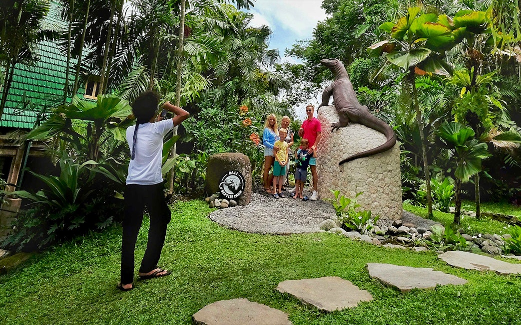 Family posing by Komodo dragon statue at Bali Reptile Park.