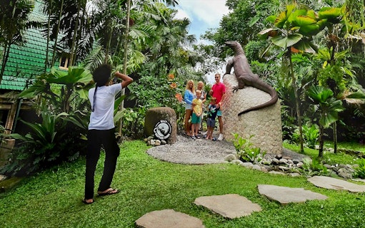 Family posing by Komodo dragon statue at Bali Reptile Park.