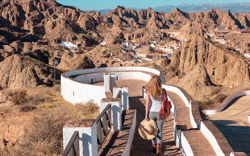 Woman walking along a path in Guadix with cave houses and desert landscape in the background.
