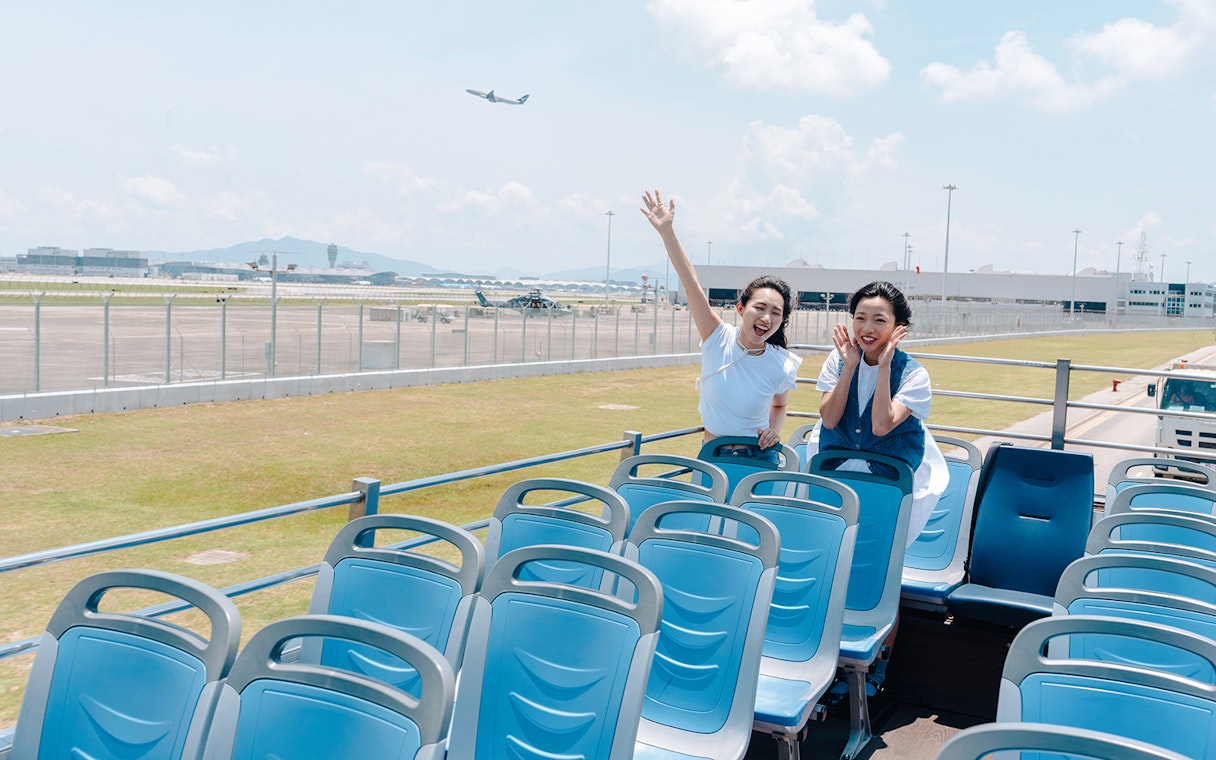 Tourists enjoying Lantau Island hop-on hop-off bus with airport view.
