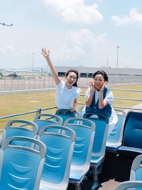 Tourists enjoying Lantau Island hop-on hop-off bus with airport view.