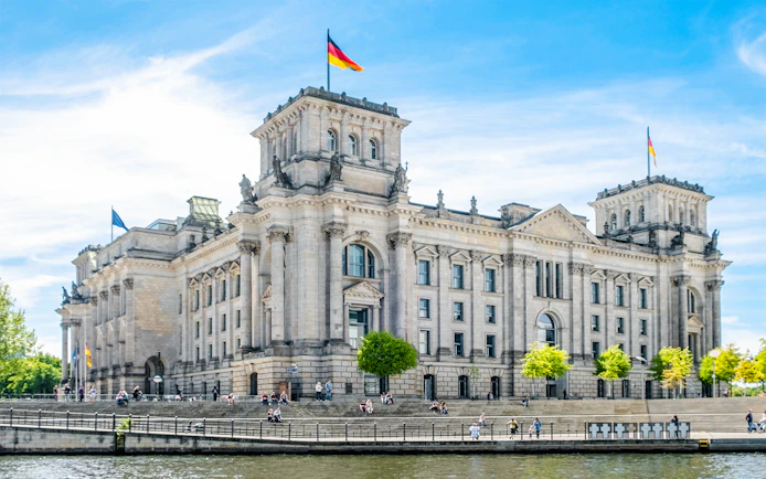 Reichstag building in Berlin with German flags and people on the steps.
