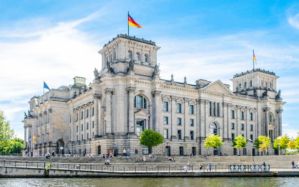 Reichstag building in Berlin with German flags and people on the steps.