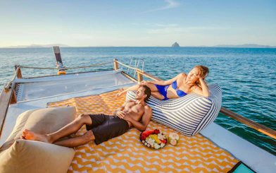 Couple relaxing on a luxury longtail boat cruise at sunset in Krabi, with fruit platter nearby.