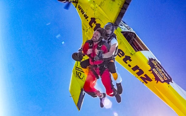 Tandem skydivers jumping from a plane over Bay of Islands, New Zealand.