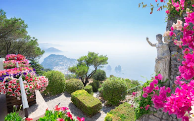 Monte Solaro view with vibrant flowers, statue, and Capri coastline.