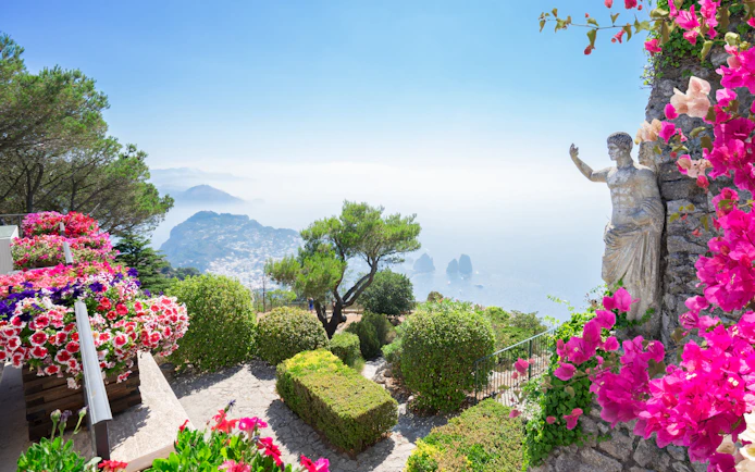 Monte Solaro view with vibrant flowers, statue, and Capri coastline.