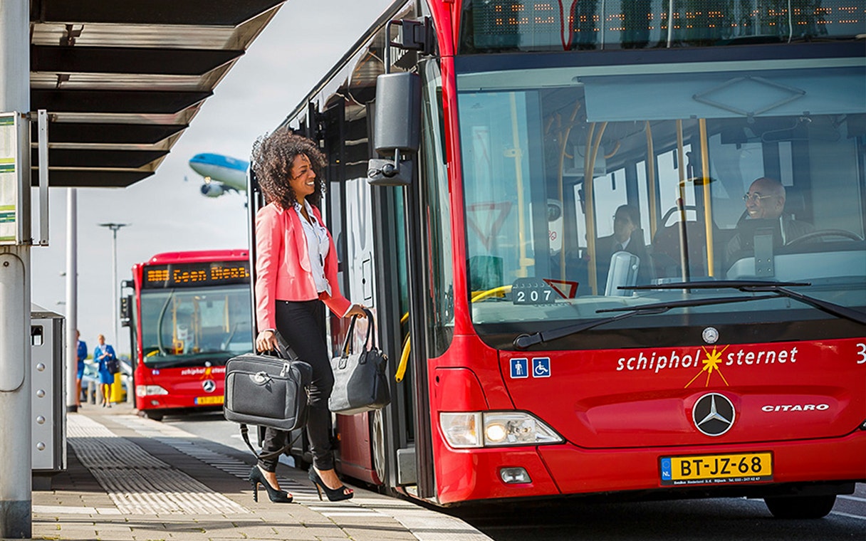 Passenger boarding red bus at Schiphol Airport for Amsterdam Airport Express route.