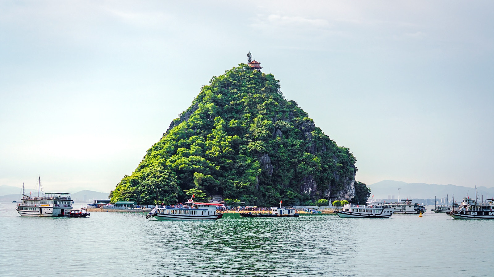 Boats near Titop Island in Ha Long Bay, Vietnam, with lush greenery and a hilltop pavilion.