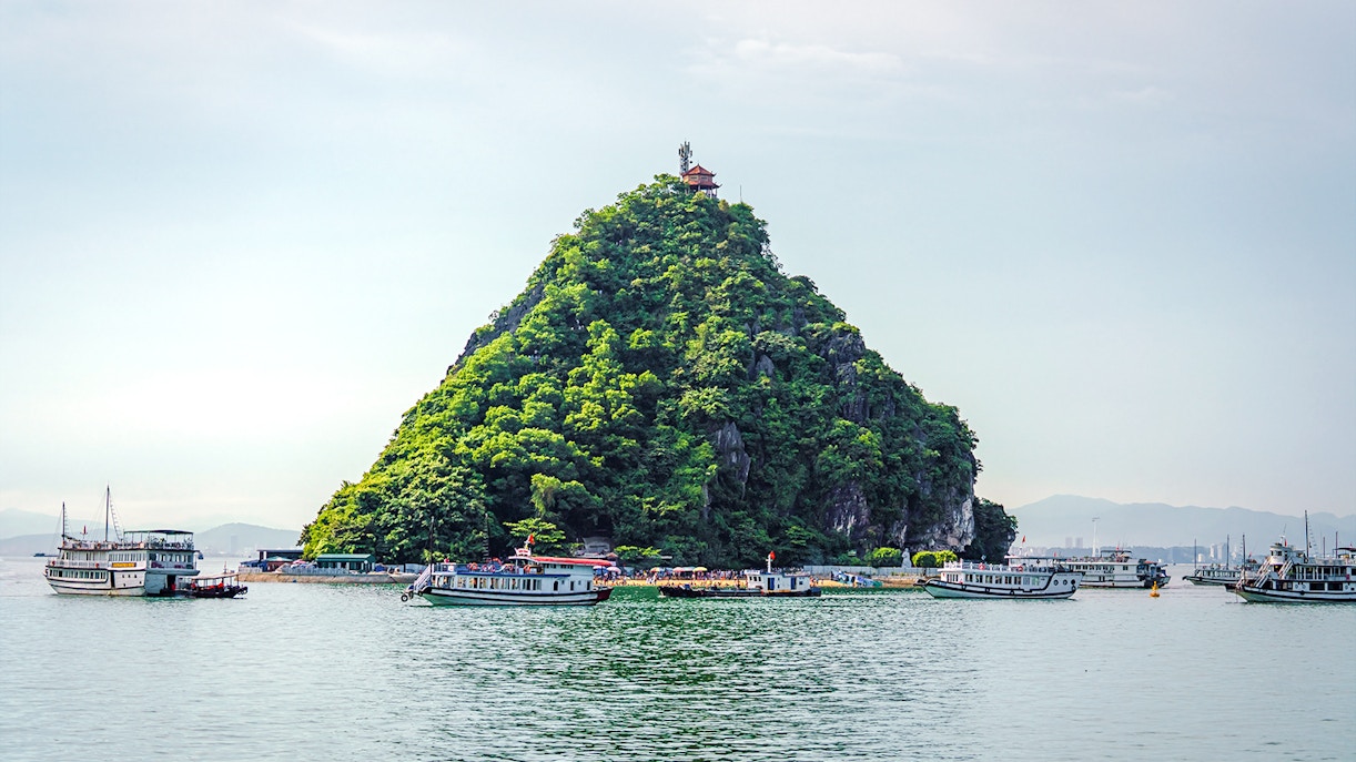 Boats near Titop Island in Ha Long Bay, Vietnam, with lush greenery and a hilltop pavilion.