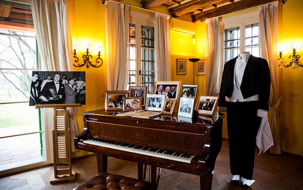 Luciano Pavarotti House Museum interior with piano, photos, and formal attire display.