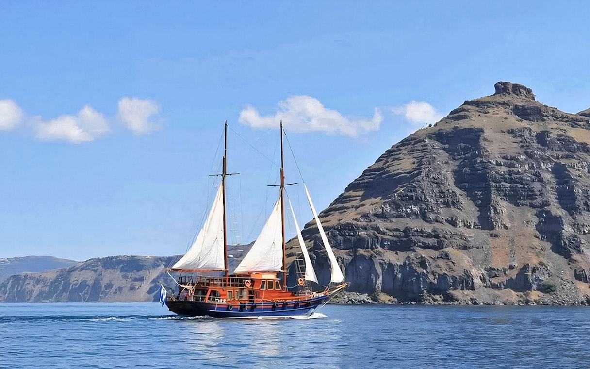 Sailing boat near volcanic cliffs on Santorini Volcanic Islands tour.