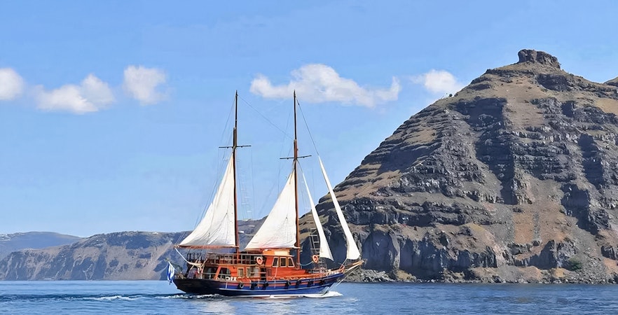 Sailing boat near volcanic cliffs on Santorini Volcanic Islands tour.