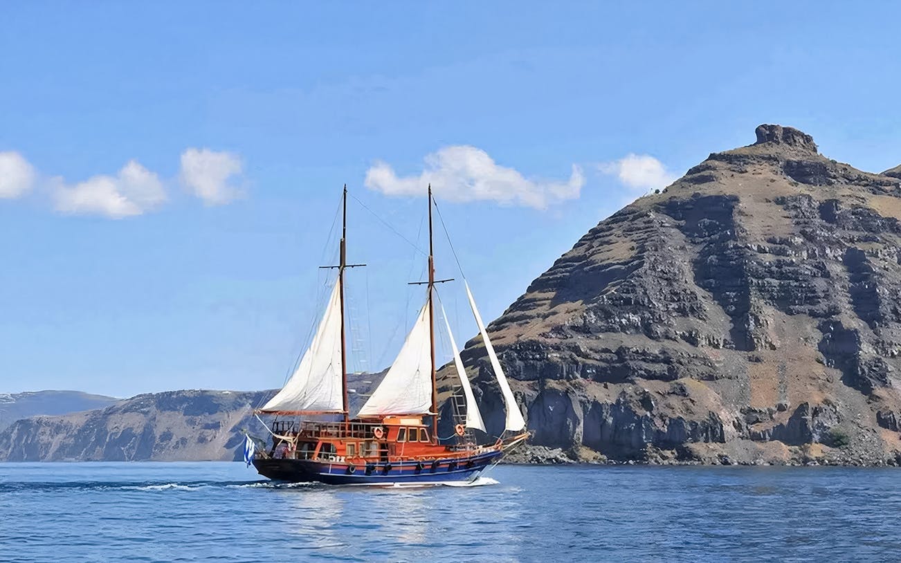 Sailing boat near volcanic cliffs on Santorini Volcanic Islands tour.