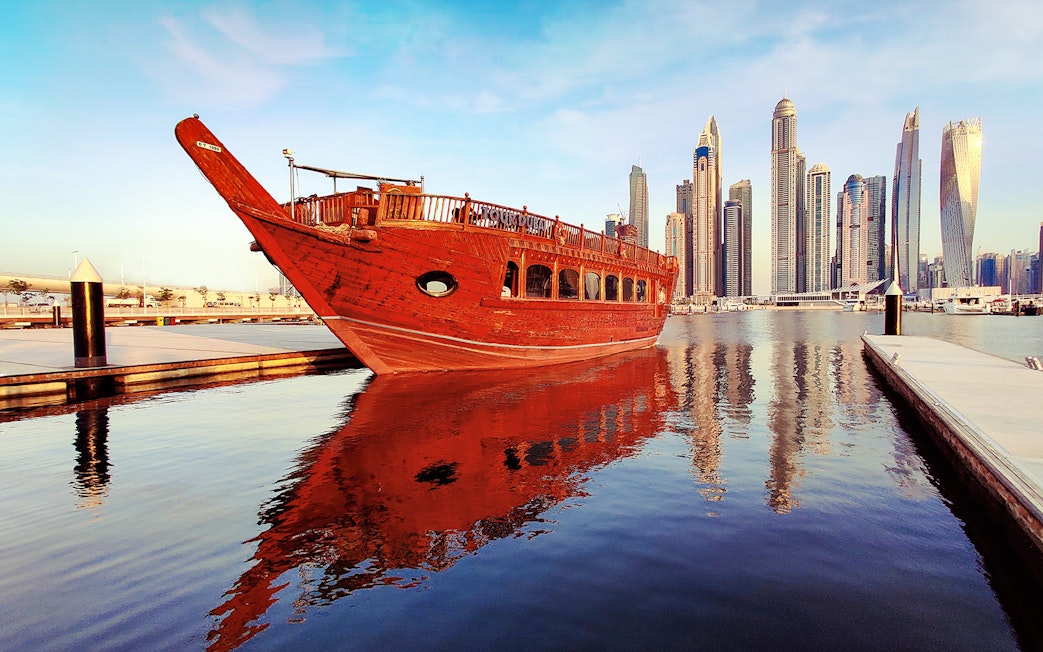Traditional dhow boat docked at Dubai Marina with skyscrapers in the background.