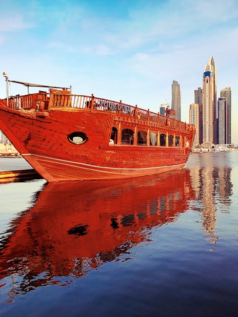 Traditional dhow boat docked at Dubai Marina with skyscrapers in the background.