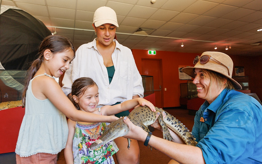 Two girls with a guide touching a young crocodile at Crocosaurus Cove, Darwin, Australia.