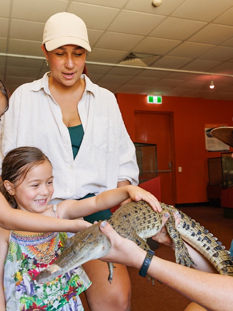 Two girls with a guide touching a young crocodile at Crocosaurus Cove, Darwin, Australia.