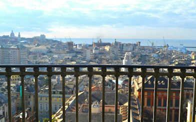 Genoa cityscape view from a balcony, featuring historic buildings and the harbor in the distance.
